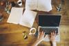 Typing at laptop with papers on desk