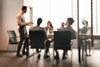 A blurred image of a team meeting taking place at the office