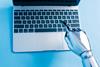 A robot hand types on a laptop keyboard