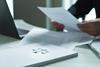 Document displaying justice scales sits on a desk as a person reads through papers in the background