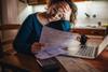 A woman reads a bill with her head in her hands