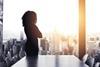 Anonymous business woman stands in an office boardroom and looks out over the city