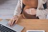 An anonymous pregnant woman sits at a desk and works from a laptop