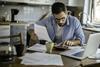 A man works through household bills using a calculator at his kitchen table