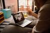 Man holds up glass of beer in front of laptop while video-calling colleagues