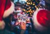 Party-goers wearing Santa hats clink glasses in front of a Christmas tree