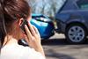 A woman speaks on the phone as she looks at the damage to her car after a crash
