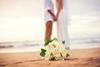 A newly-married couple hold hands on a beach as the bride's bouquet lies on the sand
