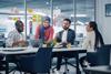 Colleagues gather around a laptop in a meeting room at the office