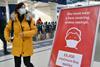 A commuter wearing a face mask walks past a sign at London Waterloo train station reminding the public they can be fined for not wearing one