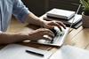 A close up of a man sat at a desk and typing on his laptop