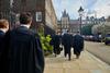 A group of barristers in robes walk together, holding their wigs