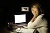 A young woman sits with her head in her hands in front of a laptop in a dark office