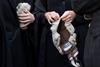 Barristers wearing gowns hold their wigs in their hands