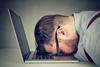 A man places his head on his laptop keyboard in despair