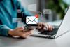 Red exclamation mark over an email symbol, with a person working on a laptop in the background