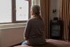 An older woman looks out of her bedroom window