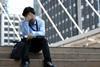 A young man sits on steps outside his office with his head in his hands