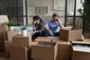 A young couple sit with their heads in their hands surrounded by moving boxes