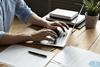 A close up of a man sat at a desk and typing on his laptop