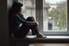 A young woman looks out of a window at home
