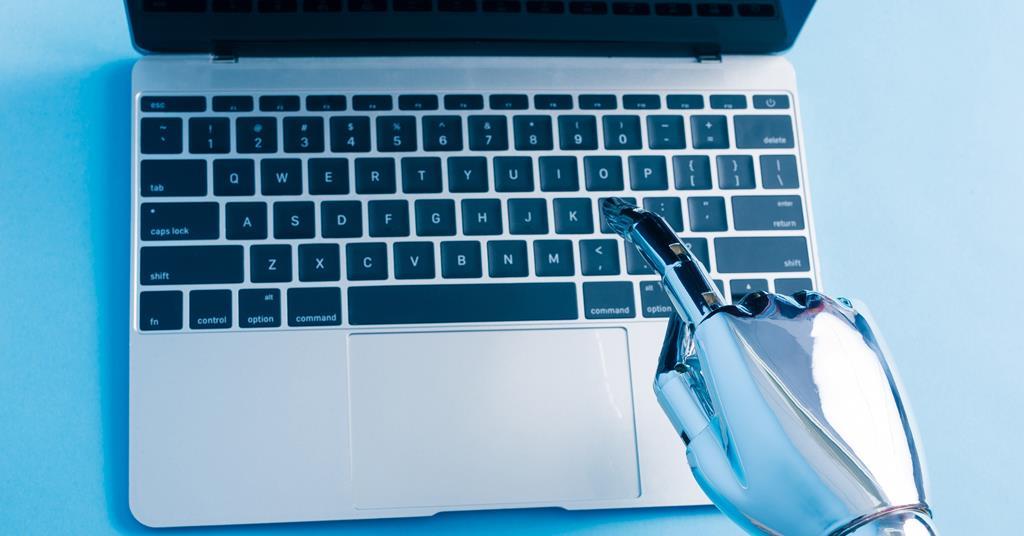 A robot hand types on a laptop keyboard