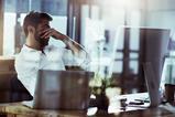 A tired man puts his hands over his eyes while sat at his desk