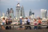 Blurred passers-by walk in front of the London City skyline