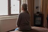 An older woman looks out of her bedroom window