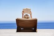 Sunbather reads book on lounger overlooking the sea