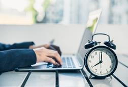 A alarm clock stands next to a laptop