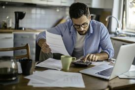 A man works through household bills using a calculator at his kitchen table