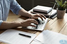 A close up of a man sat at a desk and typing on his laptop