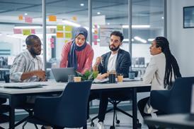 Colleagues gather around a laptop in a meeting room at the office