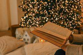 An open book is held in front of a Christmas tree