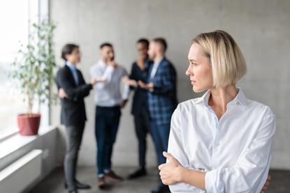 A woman stands away from a group of colleagues as they talk in the background