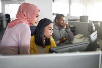 A young office worker helps out a colleague at a computer
