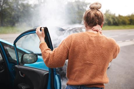 A woman steps out of her car after a crash, holding her neck in pain