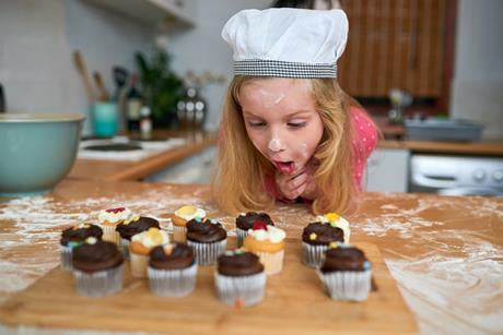 A young girl admires freshly baked cupcakes