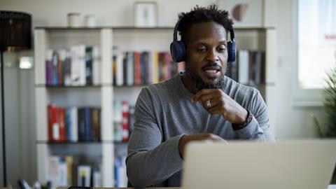 A man wearing headphones talks on a video call at home