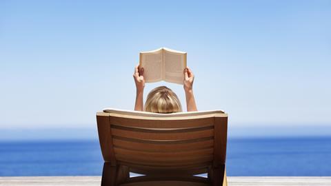 Sunbather reads book on lounger overlooking the sea