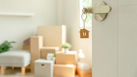 A house keyring hangs from a key in a lock, showing moving boxes behind the open door