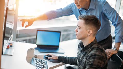 A senior colleague trains a younger office worker