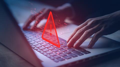 Cyber security concept image. Red warning sign hovers above laptop keyboard