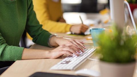 Anonymous young woman types on computer keyboard next to colleague in office