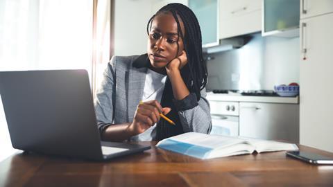 A female student sits in front of a laptop with a book open on the desk