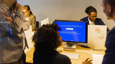 Colleagues gather round a co-worker's computer screen that displays a system error page