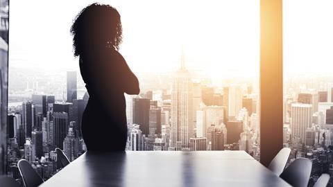 Anonymous business woman stands in an office boardroom and looks out over the city
