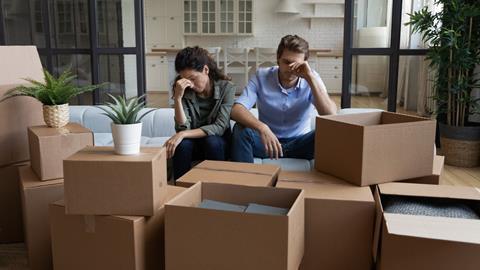 A young couple sit with their heads in their hands surrounded by moving boxes