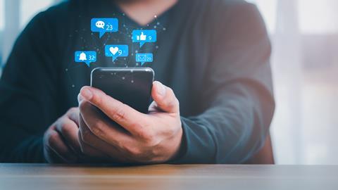 A man looks at his phone with various social media graphics appearing above the screen